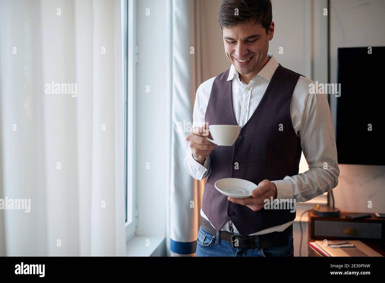 Un jeune homme lors d'un voyage d'affaires en prenant un café dans la chambre d'hôtel un beau matin. Hôtel, affaires, personnes Banque D'Images