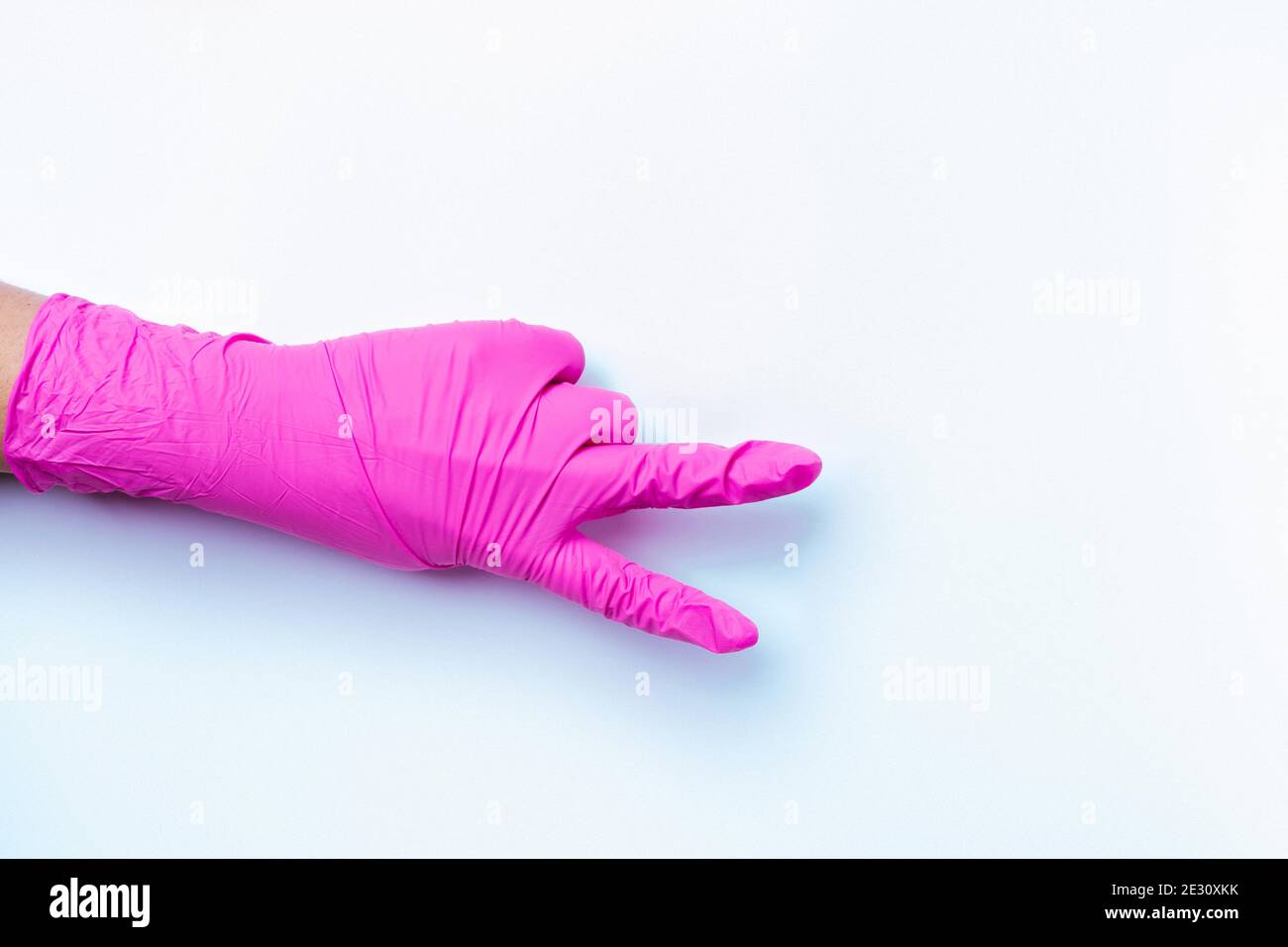 Une main paramédique dans un gant en latex rose montre le signe de victoire sur un fond blanc avec espace vide. Banque D'Images