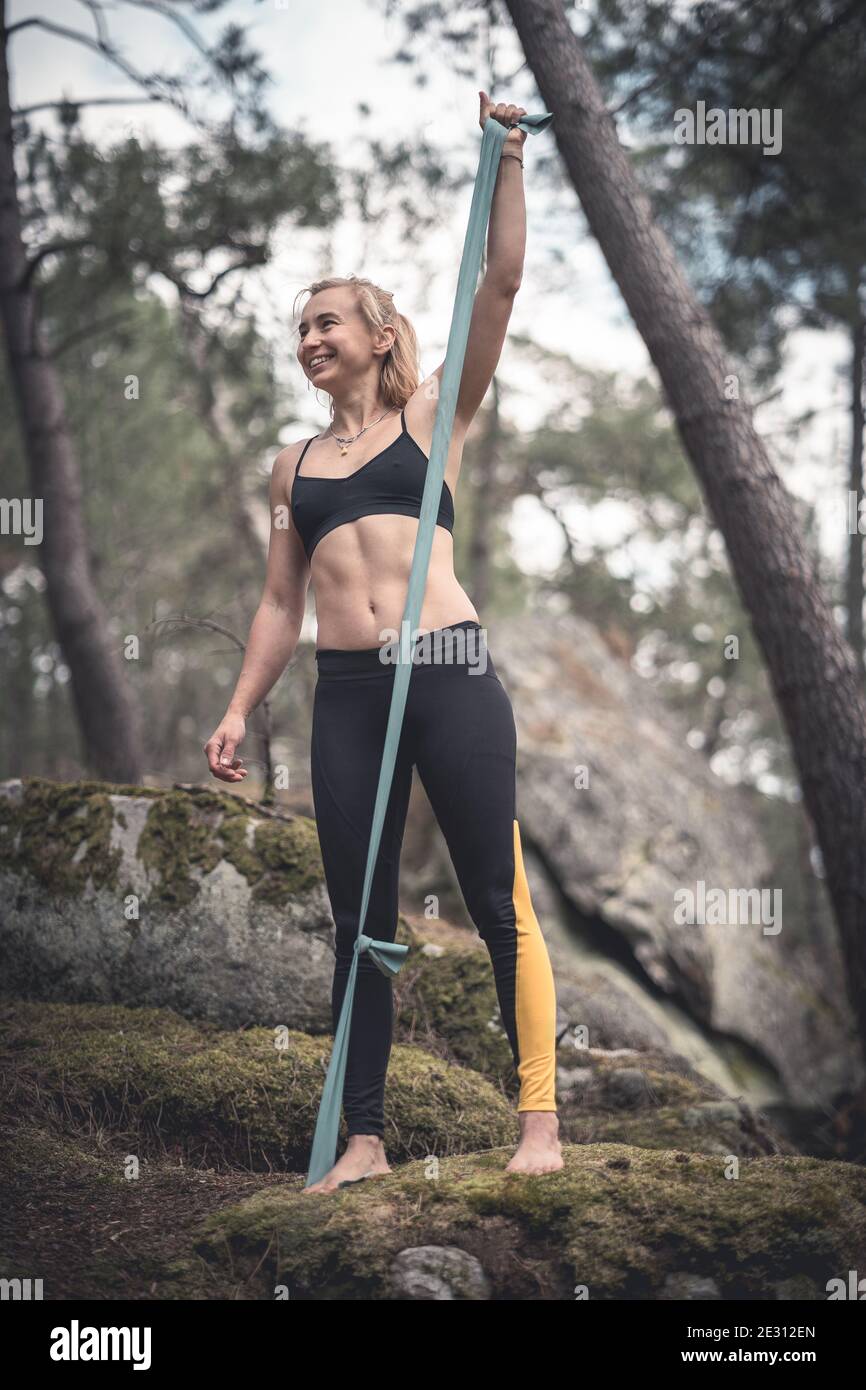 Une femme athlète portant des leggings s'exerçant pieds nus dans un forêt utilisant une bande de résistance Banque D'Images