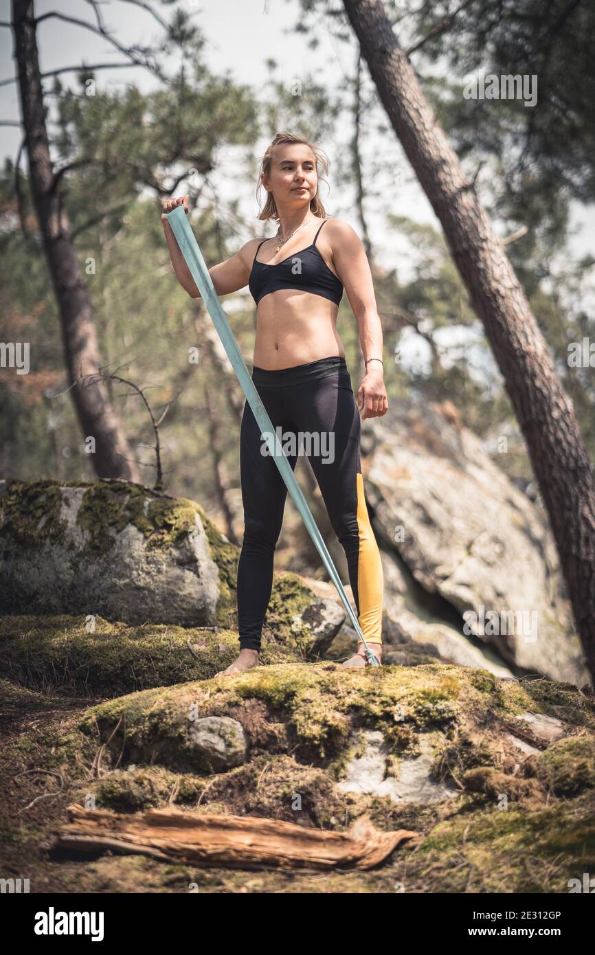 Une femme athlète portant des leggings s'exerçant pieds nus dans un forêt utilisant une bande de résistance Banque D'Images