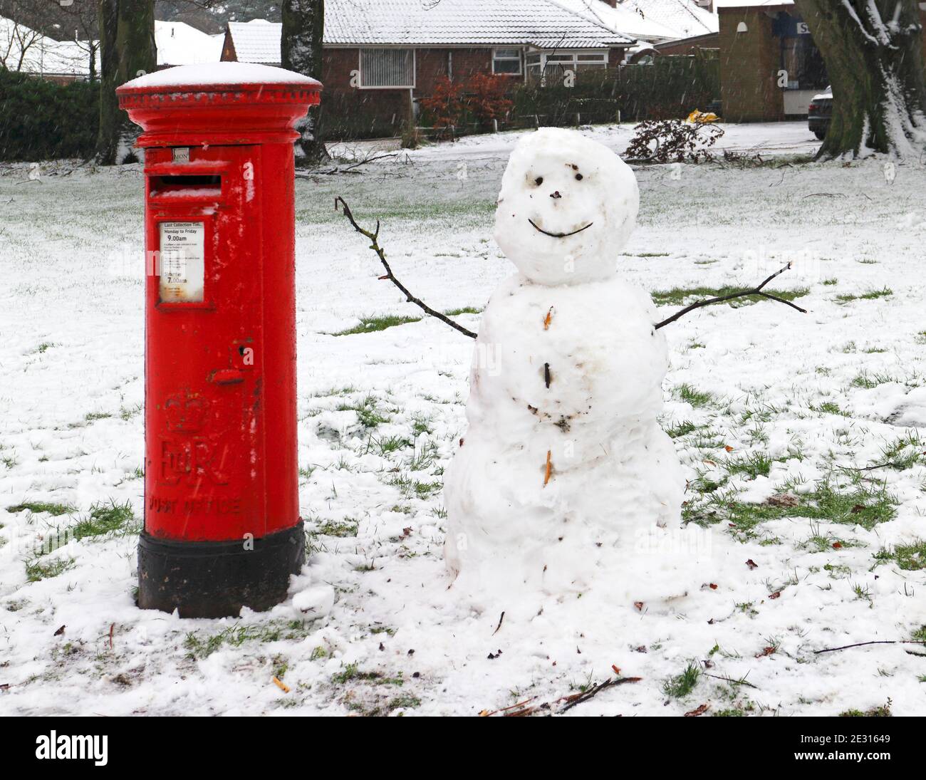 Une boîte postale rouge avec un bonhomme de neige après des averses de neige tôt le matin dans la banlieue de Norwich à Hellesdon, Norfolk, Angleterre, Royaume-Uni. Banque D'Images