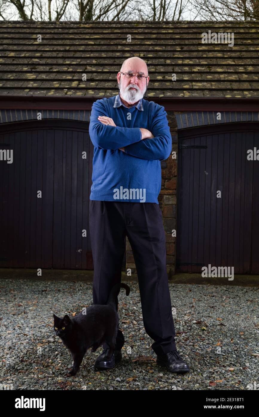 Homme âgé debout devant son garage avec son chat noir errant passé. Banque D'Images