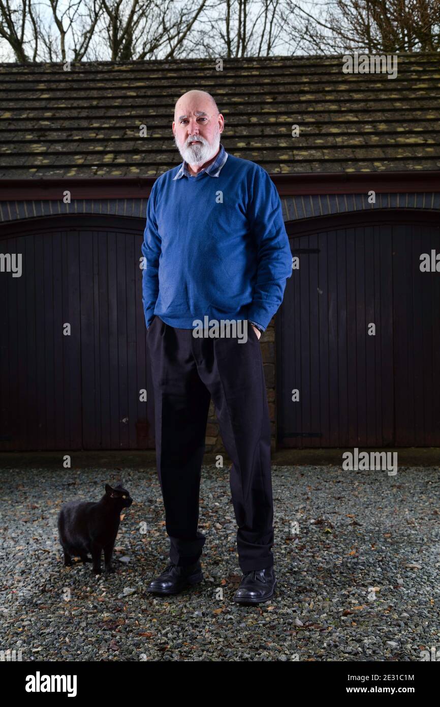 Homme âgé debout devant son garage avec son chat noir errant passé. Banque D'Images