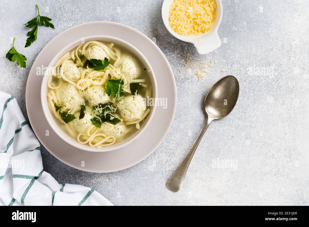 Soupe avec boulettes de poulet et pâte d'œufs, parmesan, persil dans un bol en céramique sur fond de table gris. Bouillon italien traditionnel. Vue de dessus. Banque D'Images