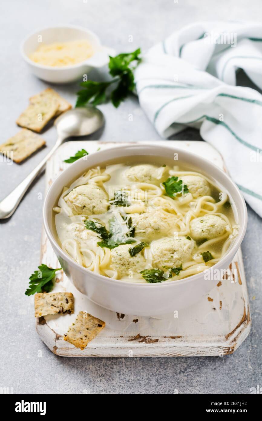 Soupe avec boulettes de poulet et pâte d'œufs, parmesan, persil dans un bol en céramique sur fond de table gris. Bouillon italien traditionnel. Vue de dessus. Banque D'Images