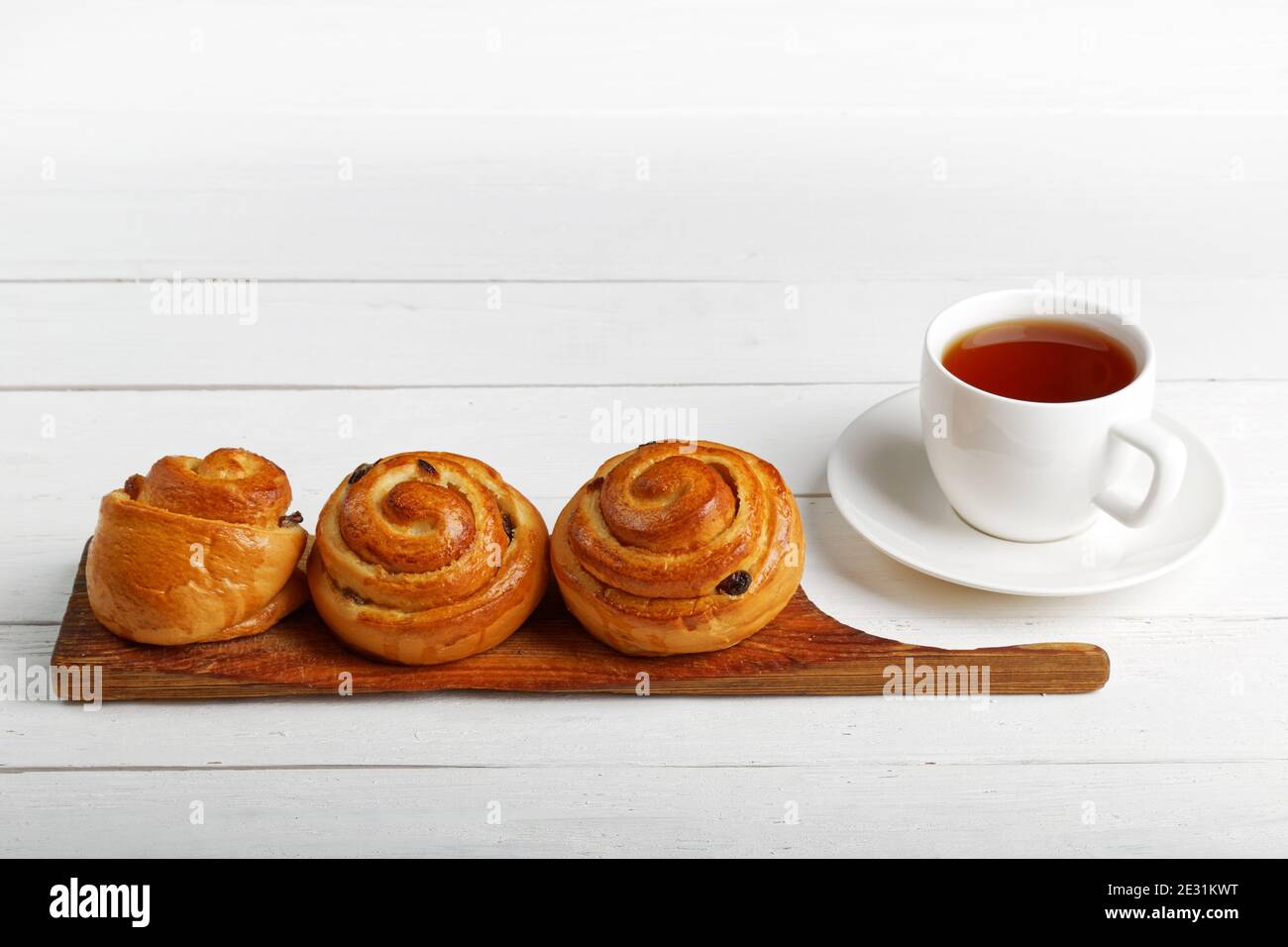 Trois petits pains aux raisins secs et une tasse de thé sur une table en bois blanc. CopySpace. Banque D'Images