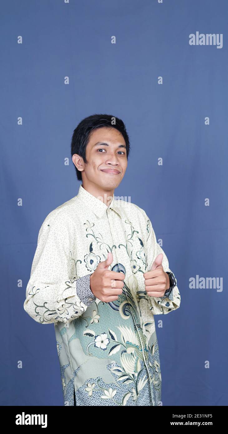 homme asiatique élégant avec des vêtements batik en studio isolé avec Fond bleu et expression OK Banque D'Images