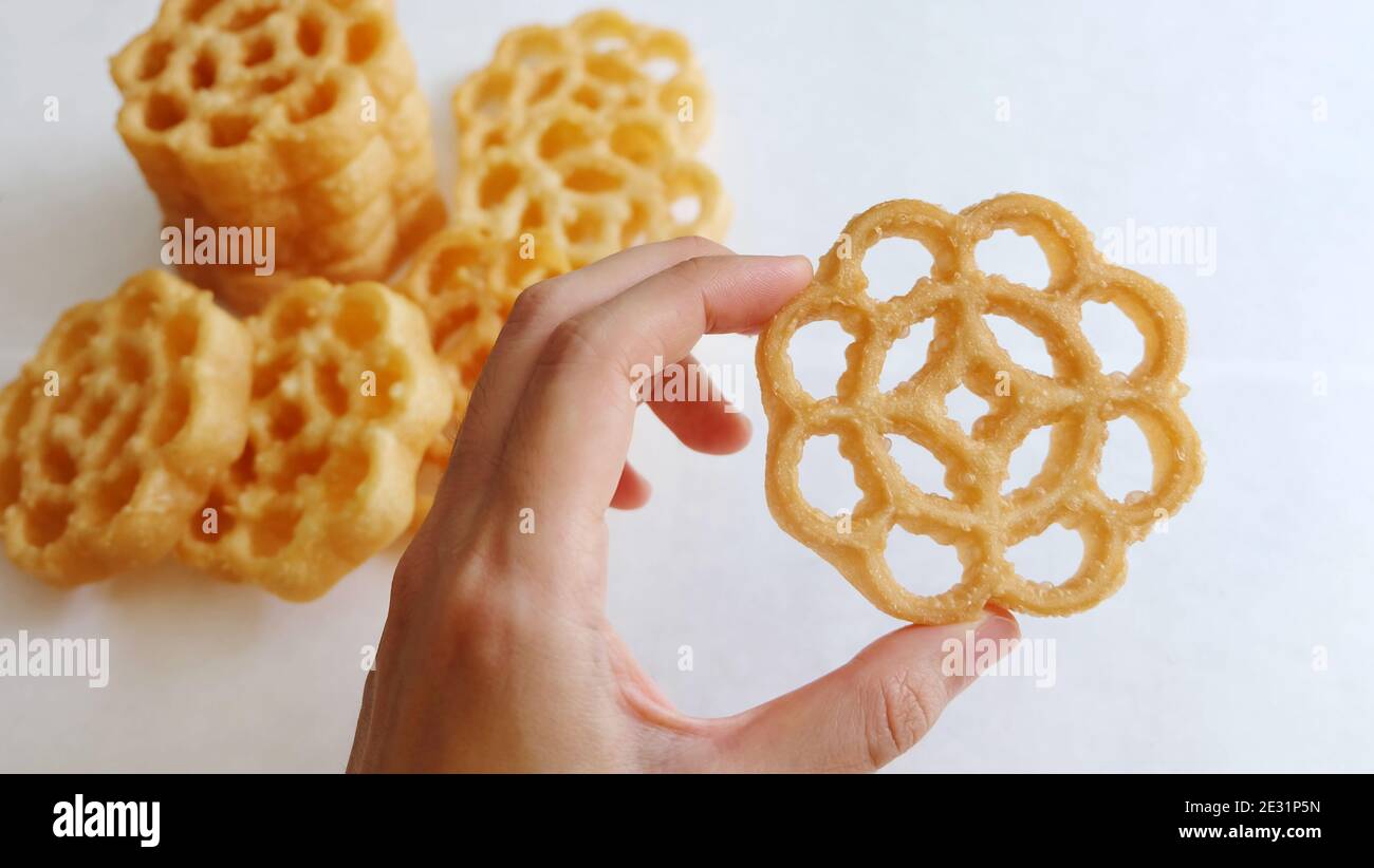 Une main tenant un biscuit en nid d'abeille, avec un peu plus en arrière-plan. Il est également connu sous le nom de kuih loyang en Malaisie, et est une collation frite populaire. Banque D'Images