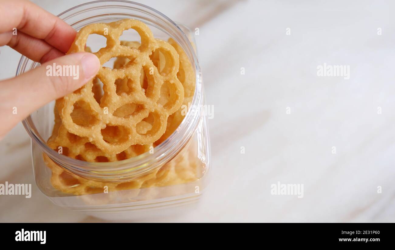 Une main prenant un biscuit en nid d'abeille, appelé kuih loyang en Malaisie. Il s'agit d'une collation frite populaire pendant les festivals. Banque D'Images