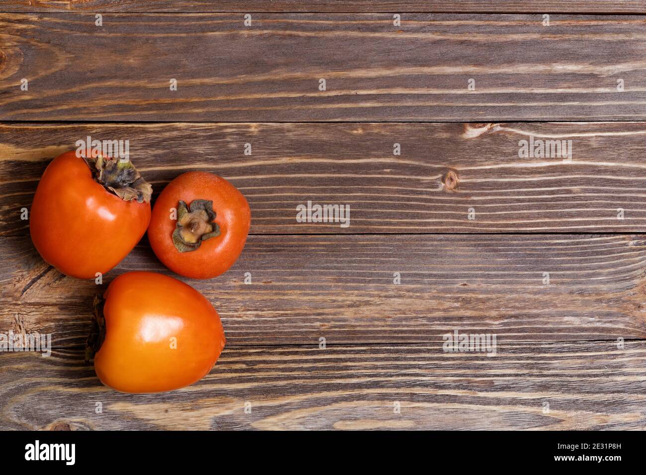 Trois persimmons isolés sur fond en bois. Vue de dessus. CopySpace. Banque D'Images