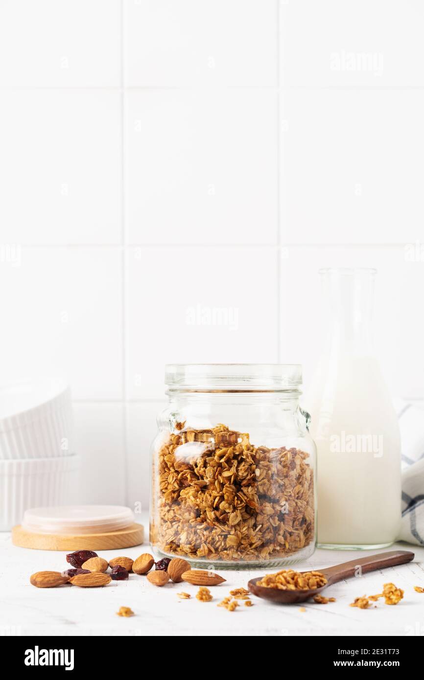 OAT granola avec une bouteille de lait, de noix et de fruits secs pour préparer un petit déjeuner sain sur une table lumineuse. Style scandinave blanc. Sélectif Banque D'Images