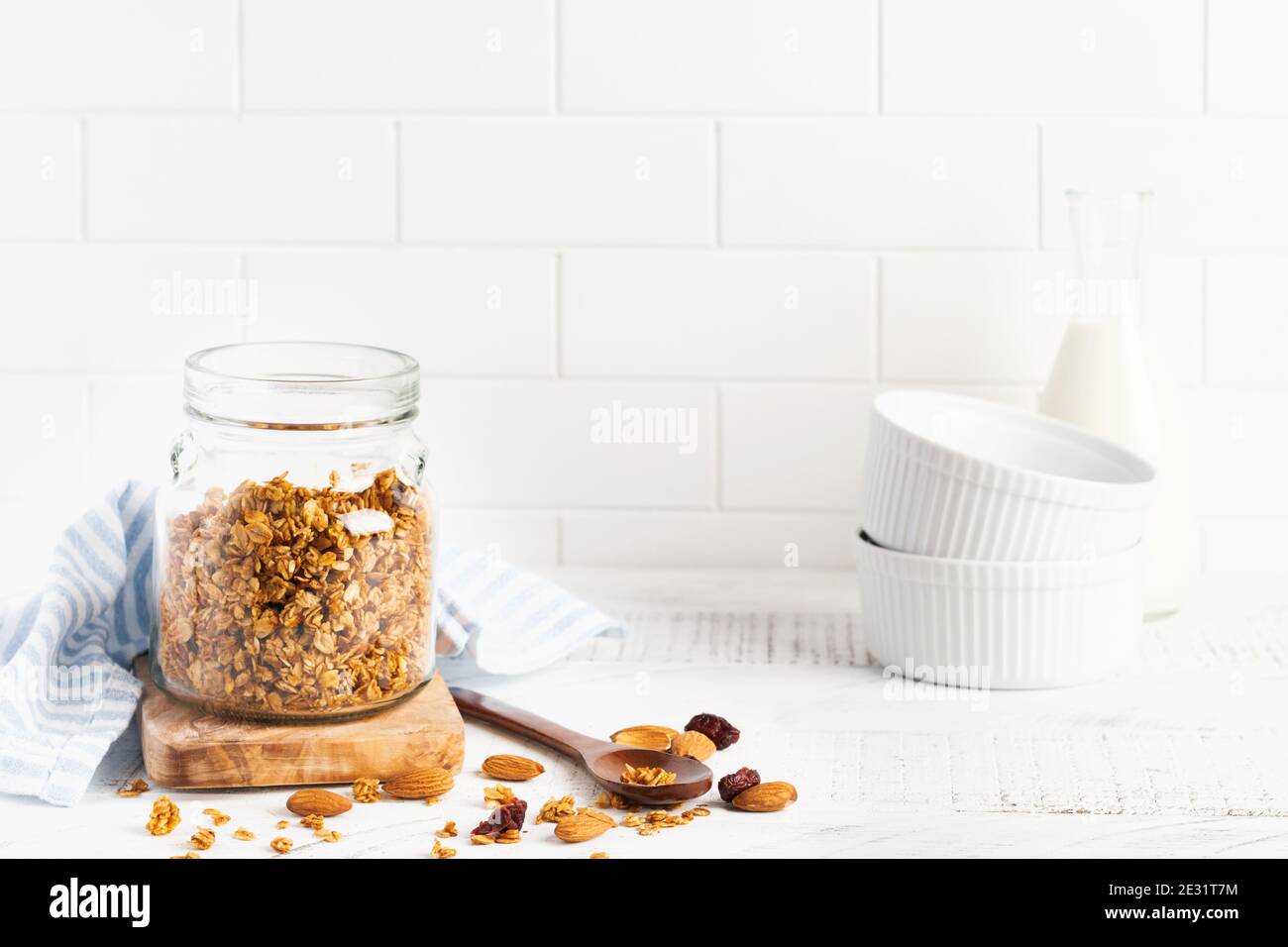 Granola d'avoine avec une bouteille de lait, de noix et de fruits secs, bols en céramique pour préparer un petit déjeuner sain sur une table lumineuse de cuisine. Merde scandinave Banque D'Images