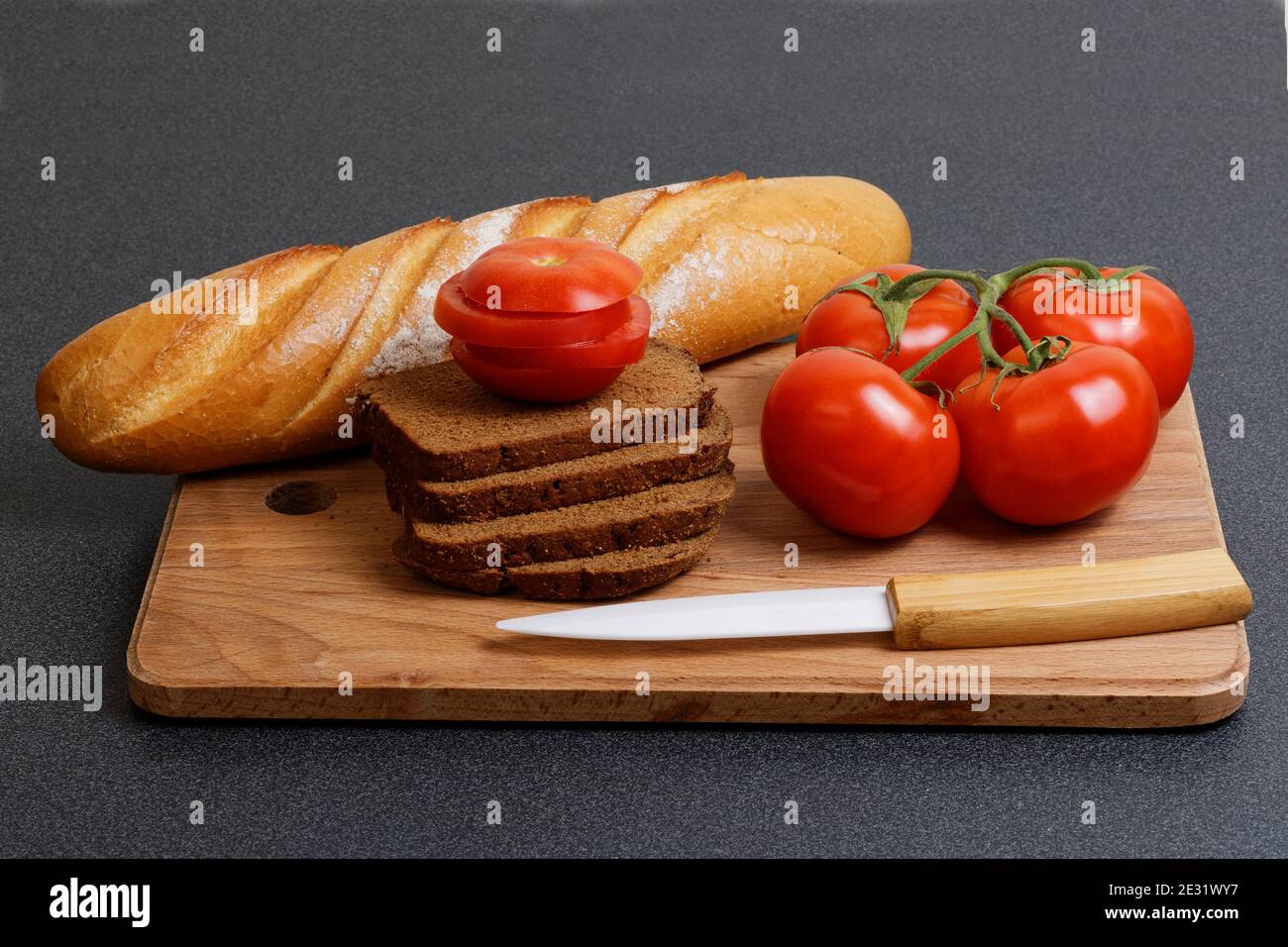 Tomate fraîche, pain et couteau sur la planche à découper de la cuisine Banque D'Images