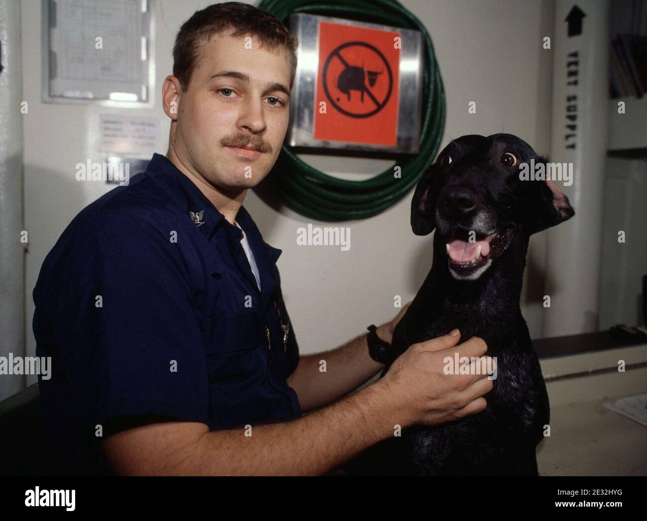 MAC, un chien de détection de stupéfiants de la US Navy, est assis avec son maître d'ouvrage à bord du porte-avions USS KITTY HAWK (CV 63). Le chien est en tournée dans l'océan Indien sur le KITTY HAWK jusqu'à son arrivée à Philadelphie en juin. Banque D'Images