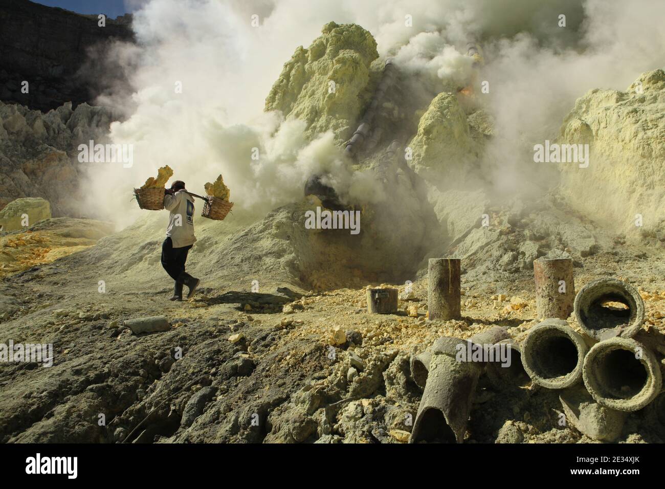 Le mineur porte les paniers avec du soufre dans les nuages de gaz volcanique dans les mines de soufre dans le cratère du volcan actif de Kawah Ijen dans l'est de Java, en Indonésie. Chaque matin, deux centaines de mineurs descendent jusqu'au fond du cratère pour la prochaine charge de soufre. Ils remplissent leurs paniers avec du soufre manuellement et portent ensuite cette lourde charge sur les pieds. Le travail extrêmement dur dans les nuages de dioxyde de soufre toxique provoque une toux dure et des yeux qui tournent presque immédiatement. Cependant, les mineurs travaillent sans protection. Peu d'entre eux ont des masques à gaz. Chaque mineur gagne environ 10 dollars américains Banque D'Images