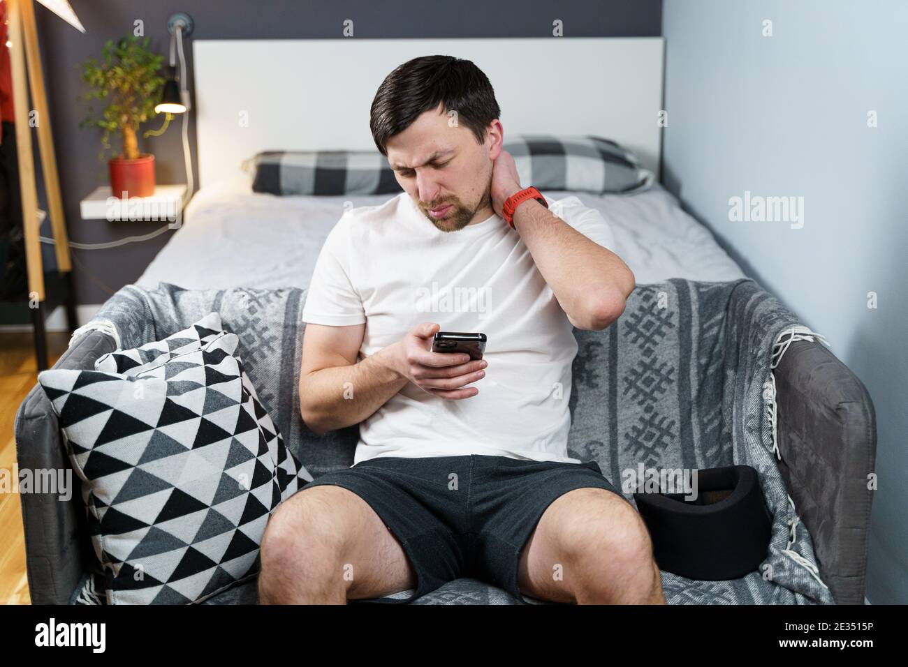 Jeune homme après un accident de voiture souffrant à la maison. Homme en mousse col cervical lisant le message sur le téléphone cellulaire, sensation de douleur dans le cou. Gars portant le cou brac Banque D'Images