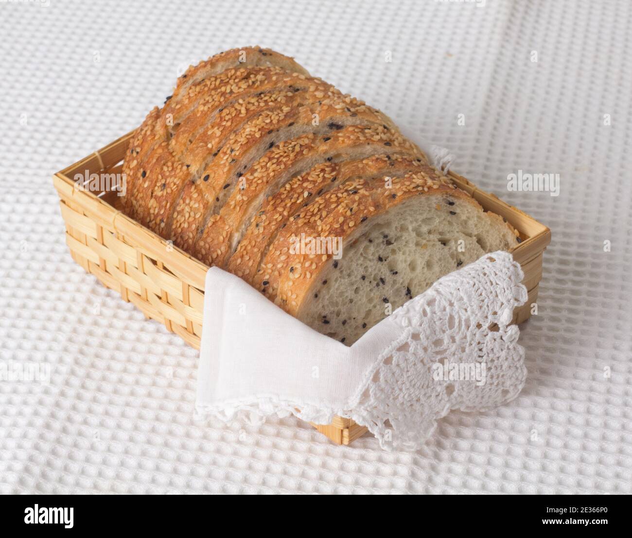 Tranches de pain au sésame dans un panier en bambou sur fond de tissu blanc Banque D'Images