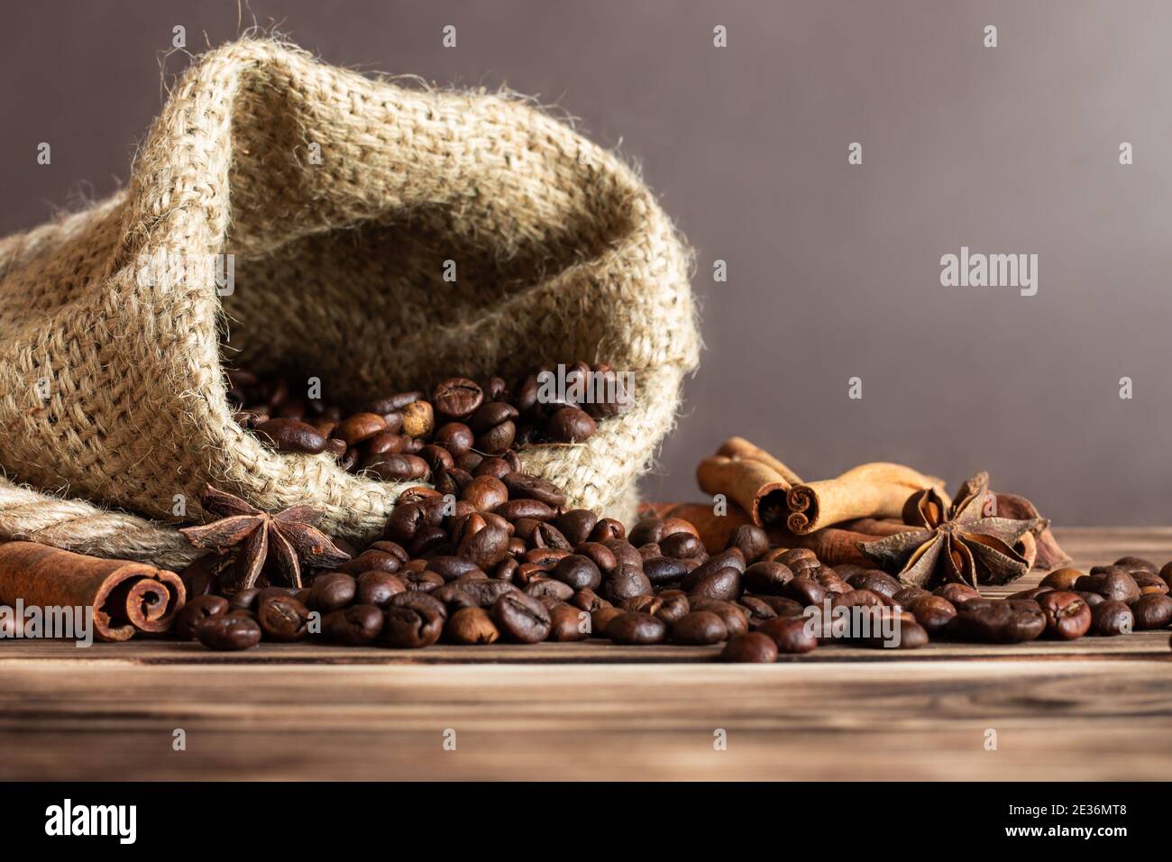 Sac en toile de jute épais avec grains de café saupoudrés sur un plan d'examen en bois brûlé avec bâtons de cannelle et étoiles anis. Copier l'espace Banque D'Images