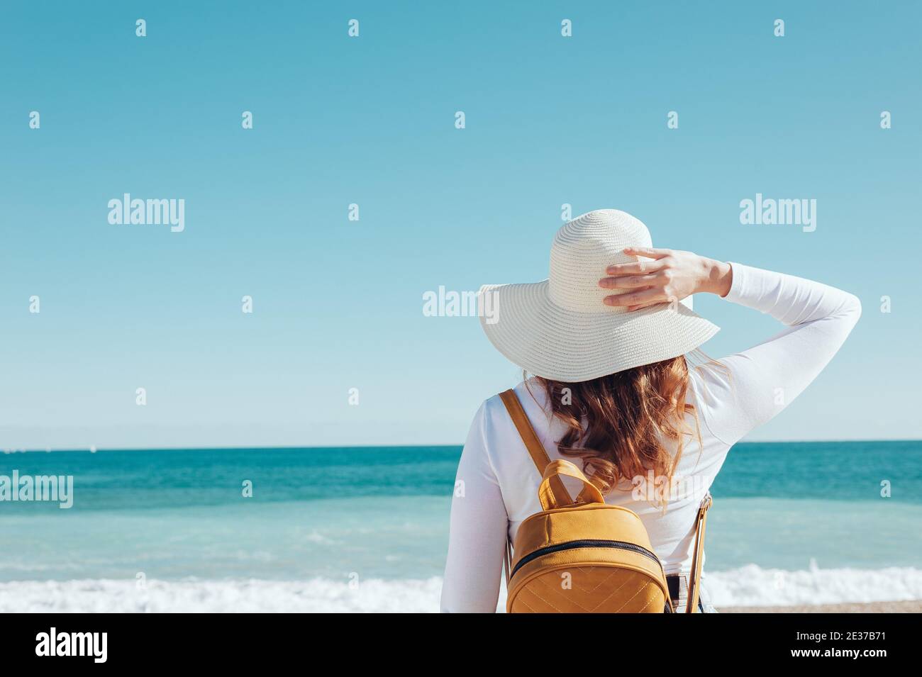 redhead femme portant un chapeau et un sac à dos jaune sur une plage turquoise méditerranéenne Banque D'Images