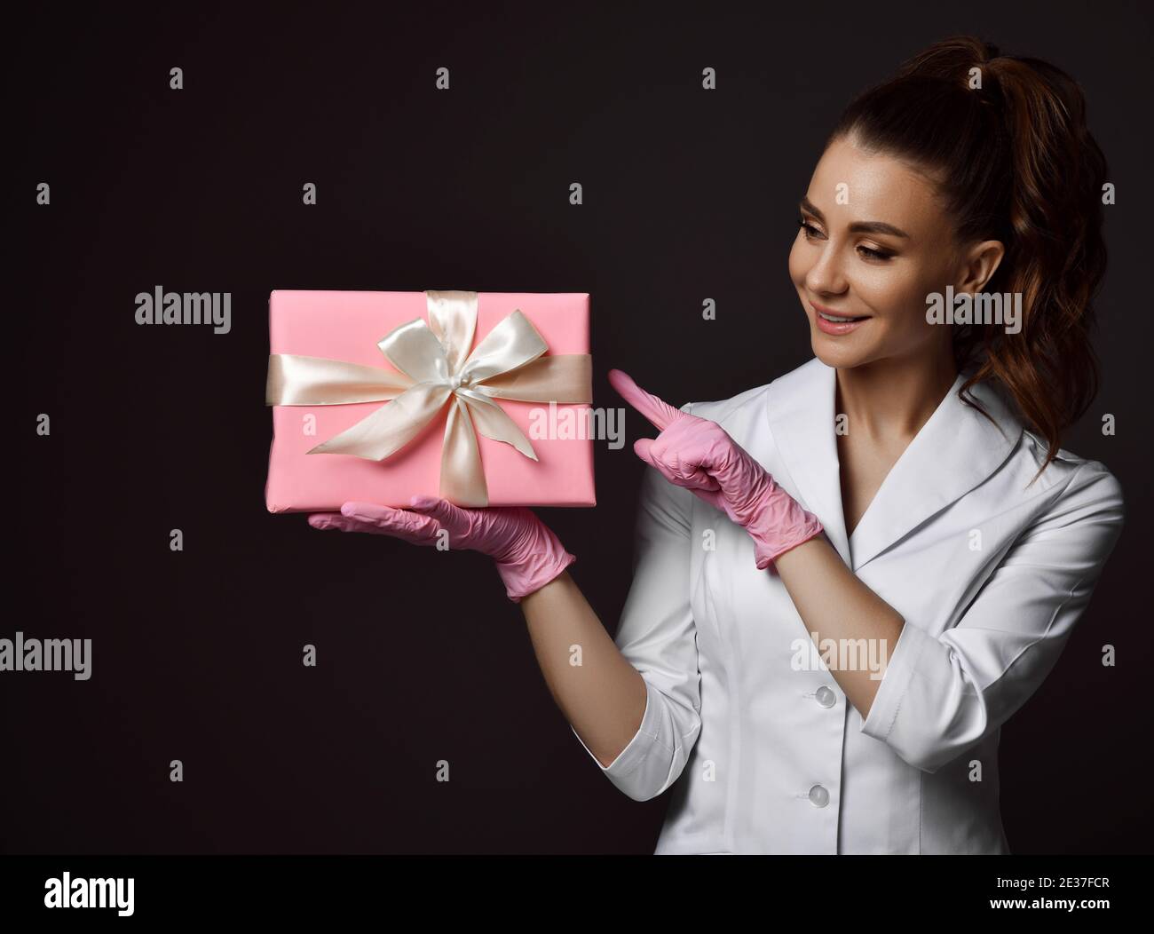 Femme médecin gynécologue reproductologue en gants de latex rose et uniforme boîte à présent de vacances debout et de maintien Banque D'Images