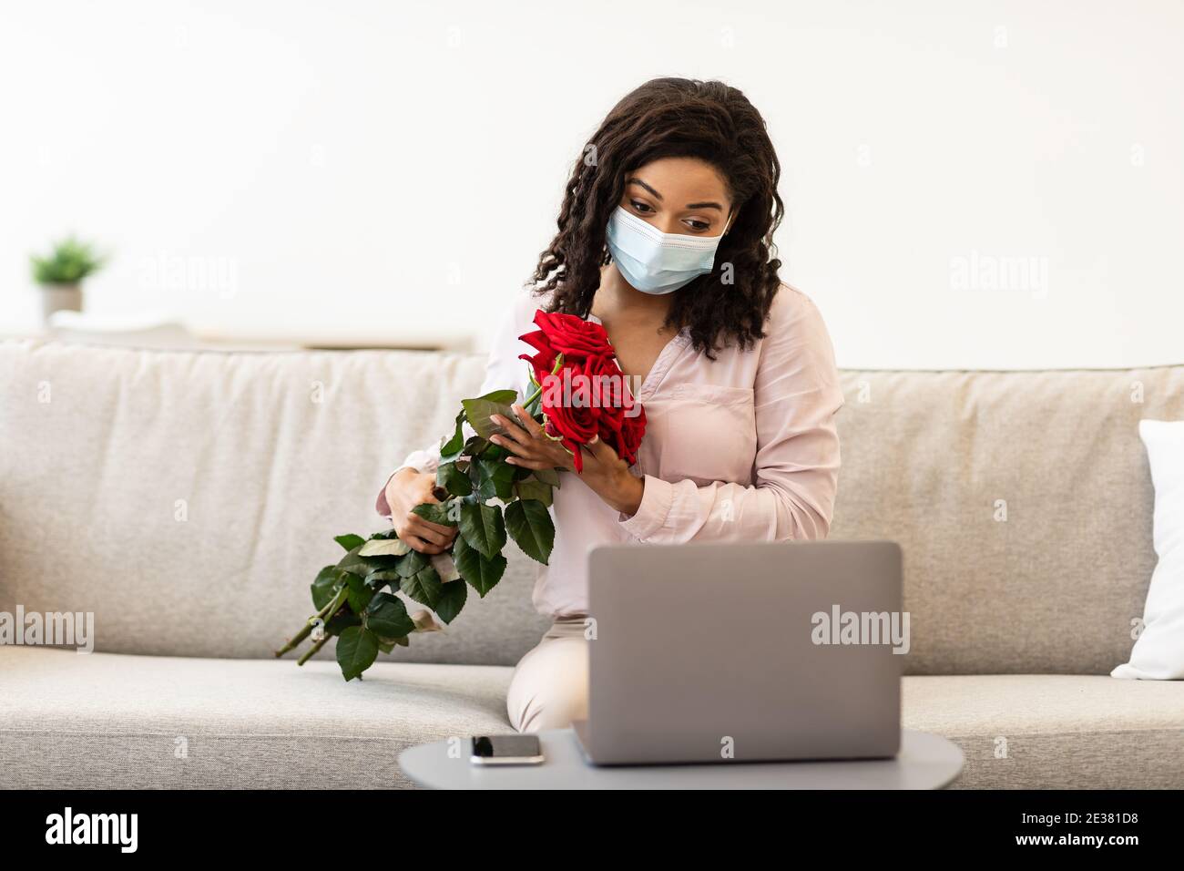 Femme afro-américaine tenant des roses rouges portant un masque Banque D'Images