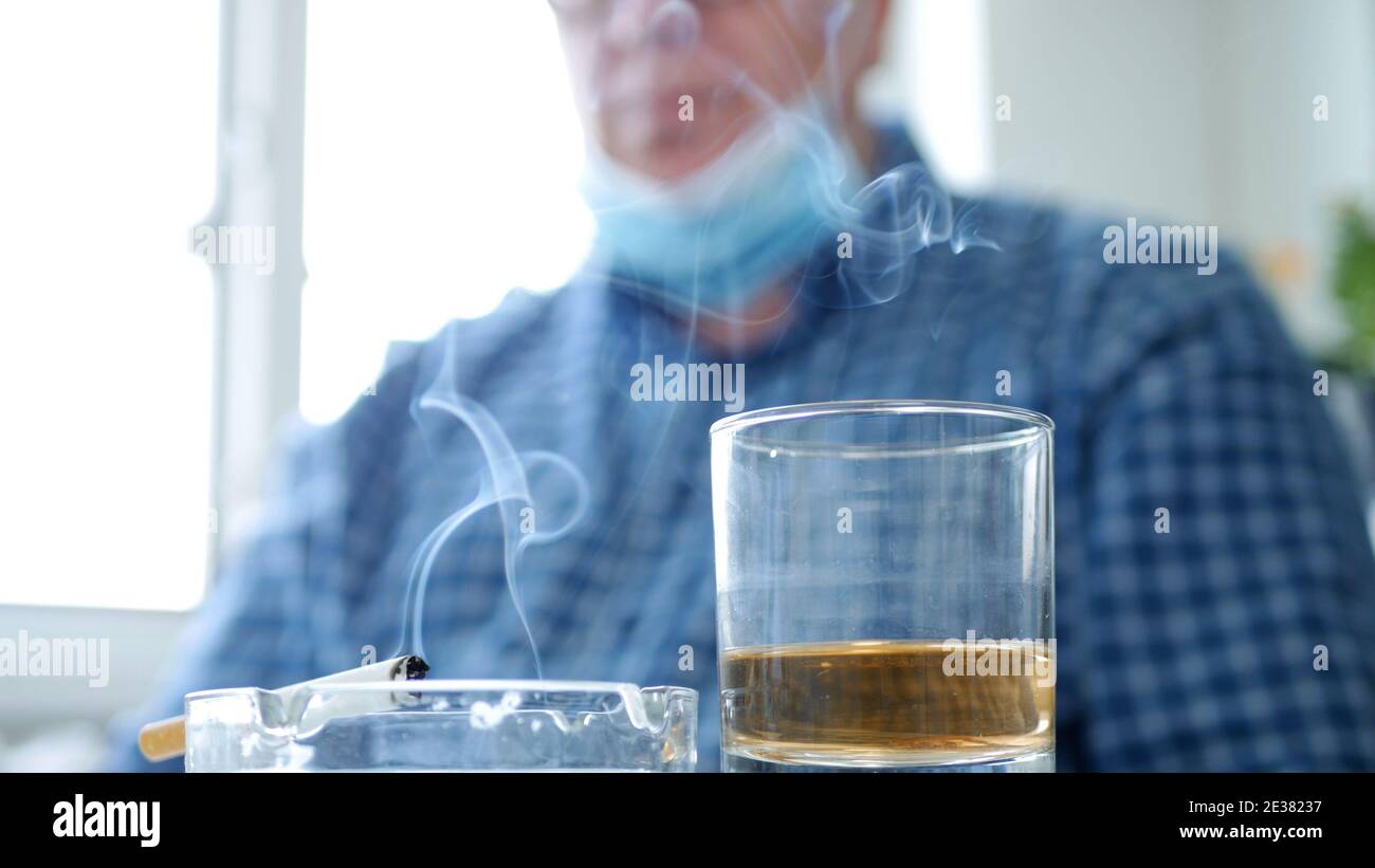 Image floue avec un homme qui boit de l'alcool et fume Une cigarette portant un masque de protection sur son masque facial Son visage Banque D'Images