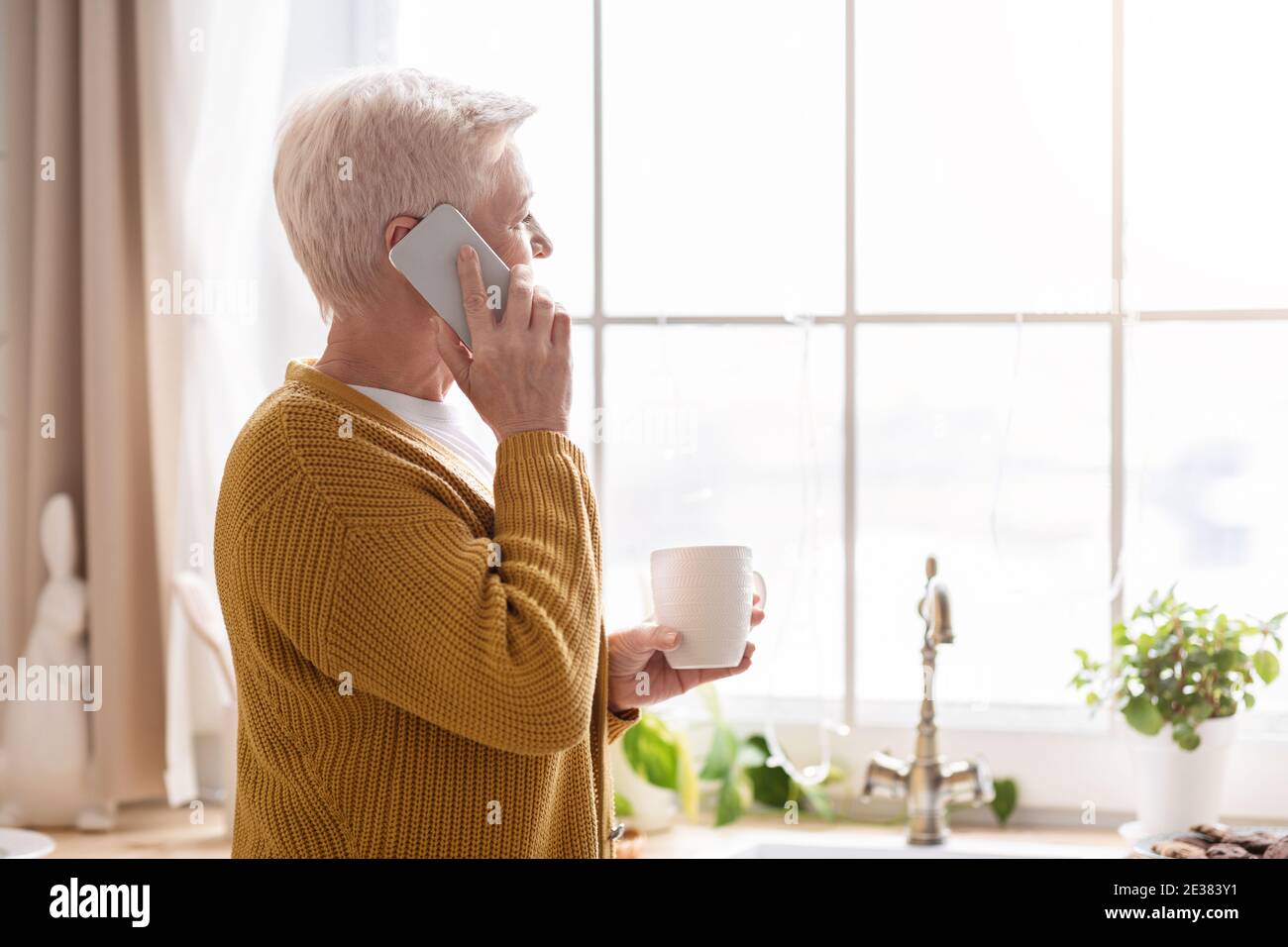 Vue latérale de la vieille dame parlant au téléphone dans la cuisine Banque D'Images