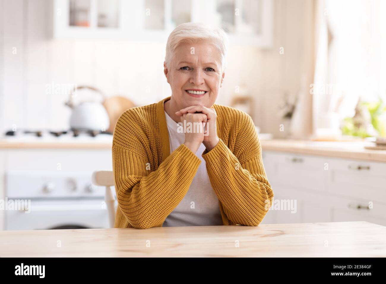 Portrait d'une vieille femme heureuse assise dans la cuisine Banque D'Images