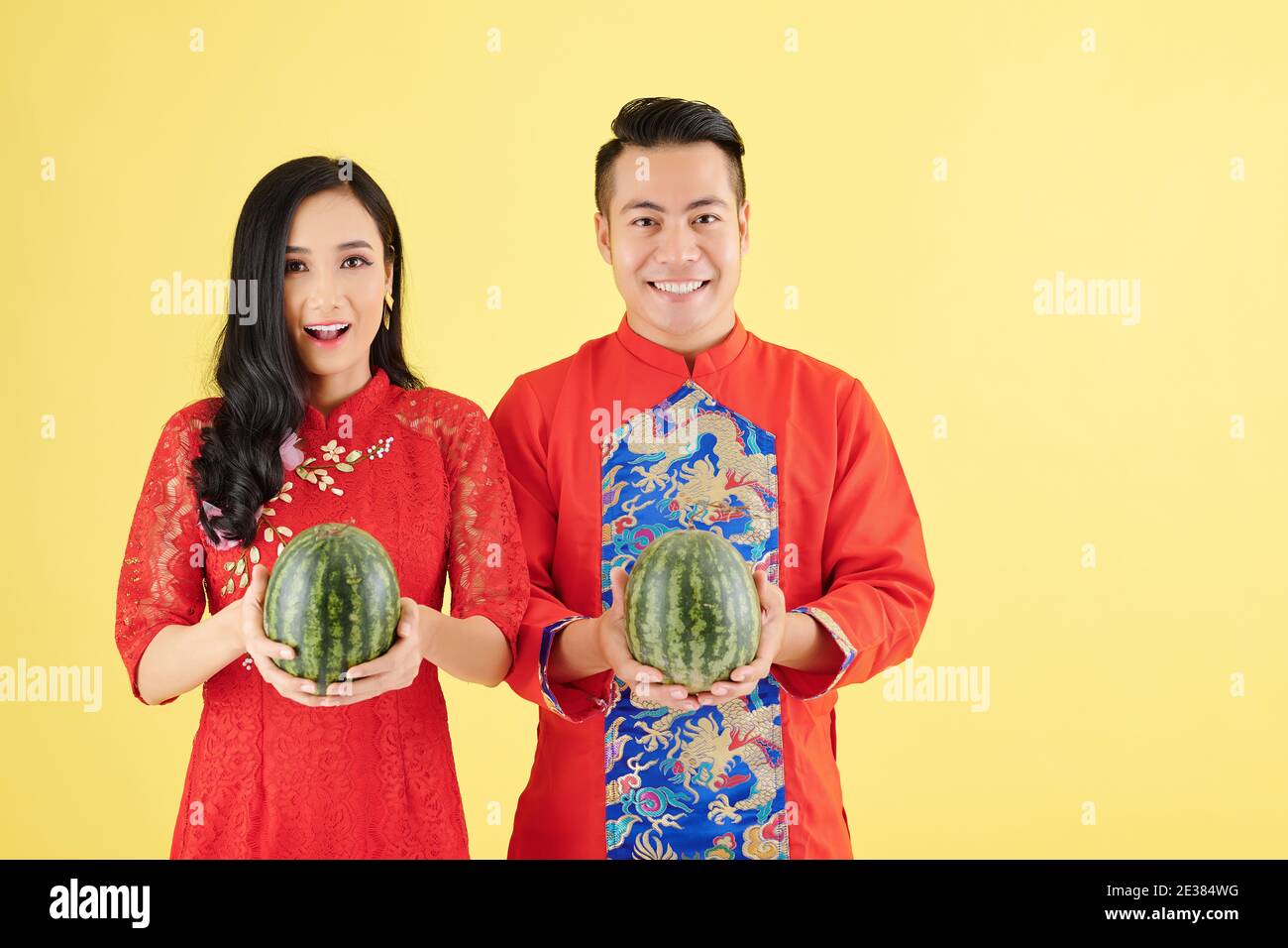 Portrait d'un jeune couple asiatique heureux dans le traditionnel Lunar New Costumes d'année contenant des pastèques fraîches et mûres Banque D'Images