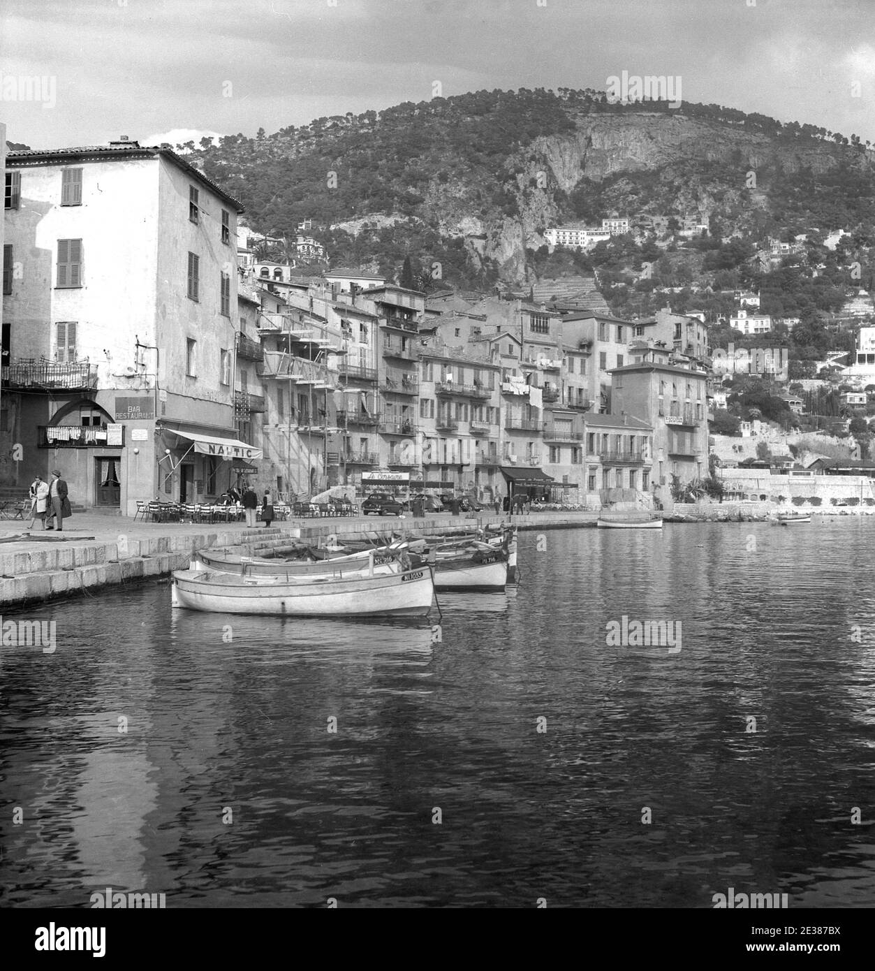 1950s, historique, vue sur le joli village côtier de Villefranche-sur-Mer dans le sud de la France à cette époque. Vieille ville pittoresque située dans la région des Alpes-Côte d'Azur sur la Côte d'Azur, Villefranche est considérée comme l'une des plus belles baies du monde et entourée par le Cap de Nice et le Cap Ferrat. On voit sur la photo le bar/restaurant, Nautic et le port clos. Banque D'Images