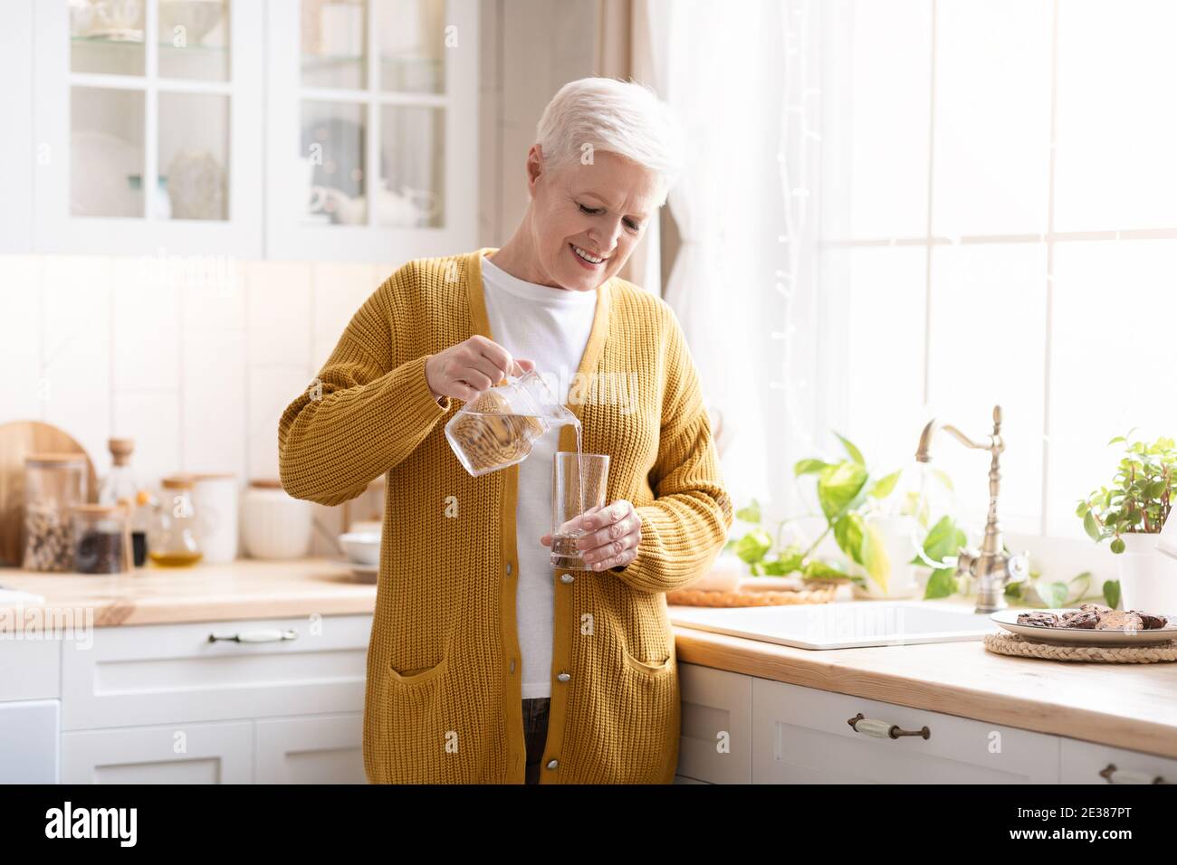 Belle-mère verser de l'eau dans le verre dans la cuisine à la maison Banque D'Images