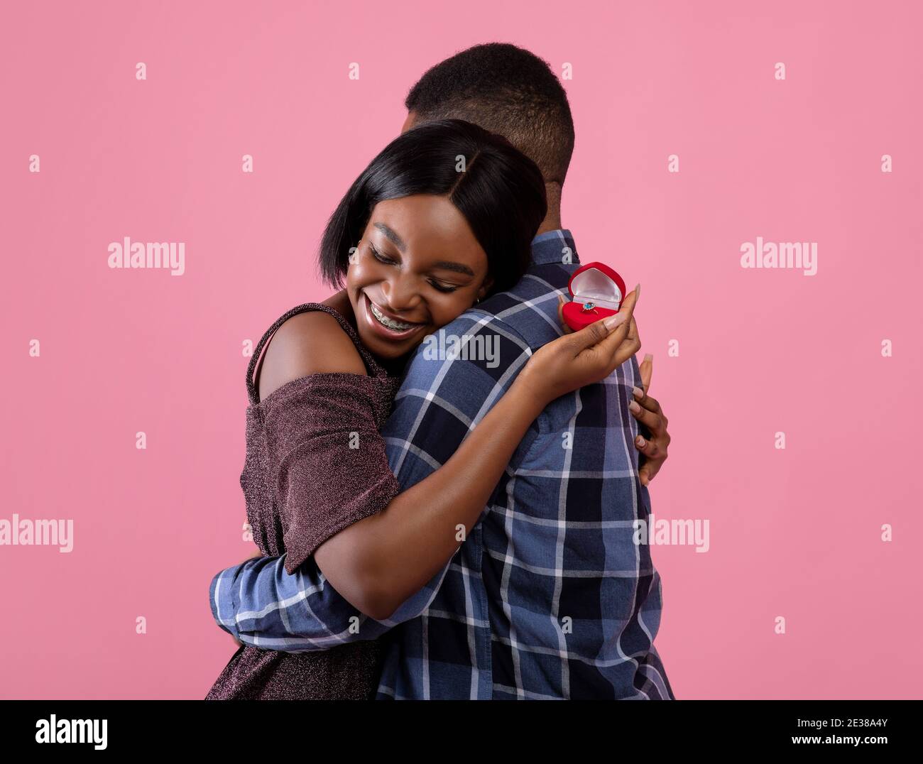 Femme noire avec anneau d'engagement embrassant son futur mari, en disant OUI à sa proposition de mariage sur fond rose Banque D'Images