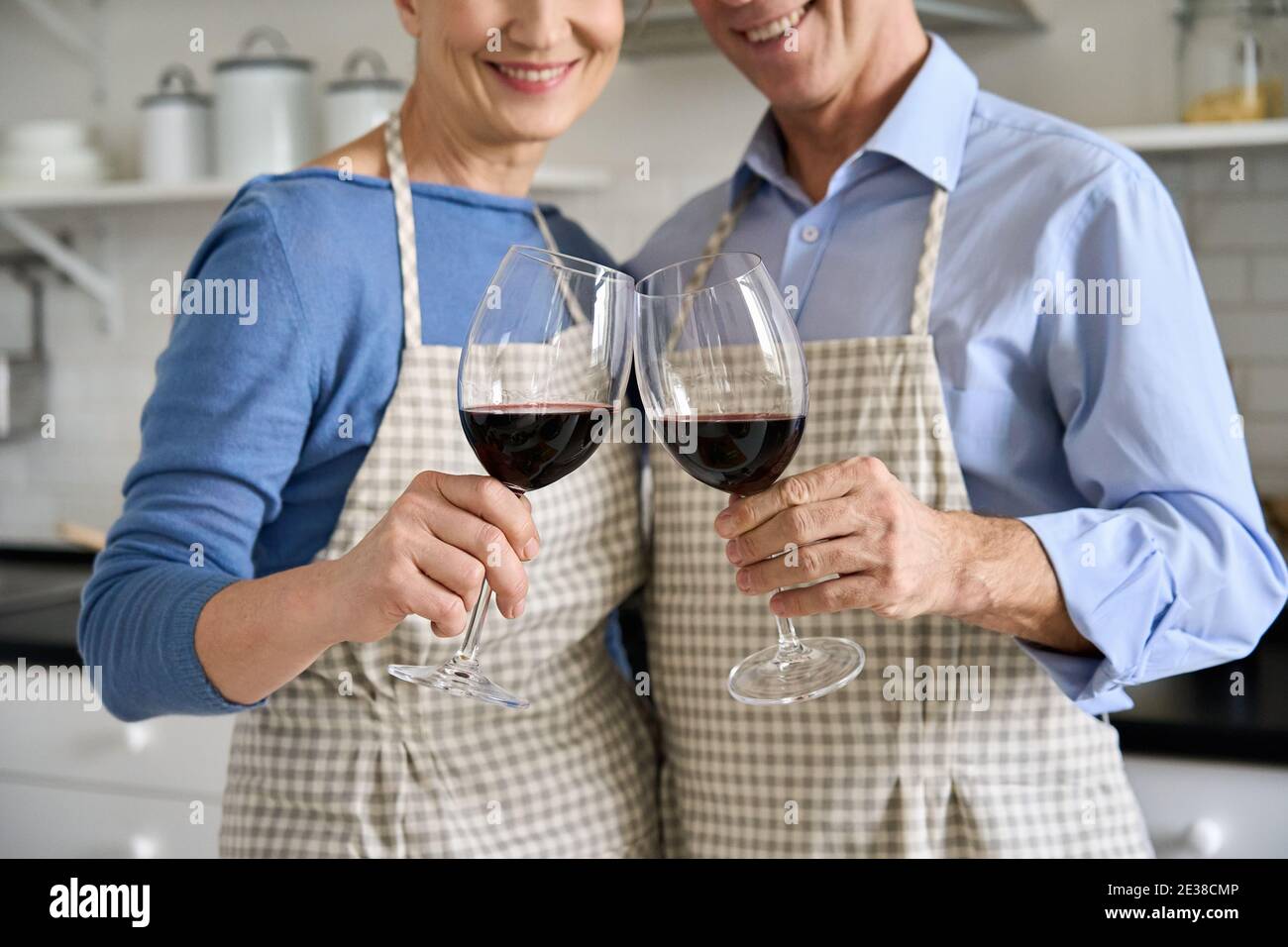 Joyeux couple senior tenant des verres de vin buvant debout dans la cuisine, gros plan. Banque D'Images