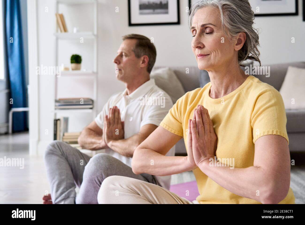 Calme sain vieux couple méditer avec les yeux fermés main namaste à la maison ensemble. Banque D'Images