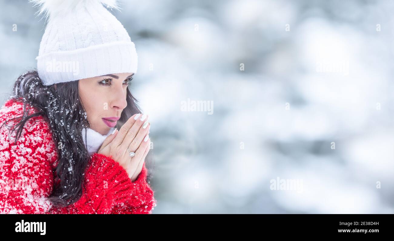 Une femme respire de l'air chaud de sa bouche aux mains lors d'une journée hivernale glaciale à l'extérieur. Banque D'Images