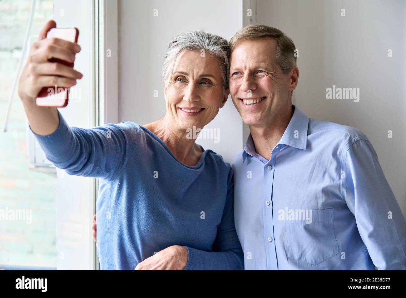 Heureux couple d'âge moyen tenant un smartphone pour prendre des photos de selfie à la maison. Banque D'Images