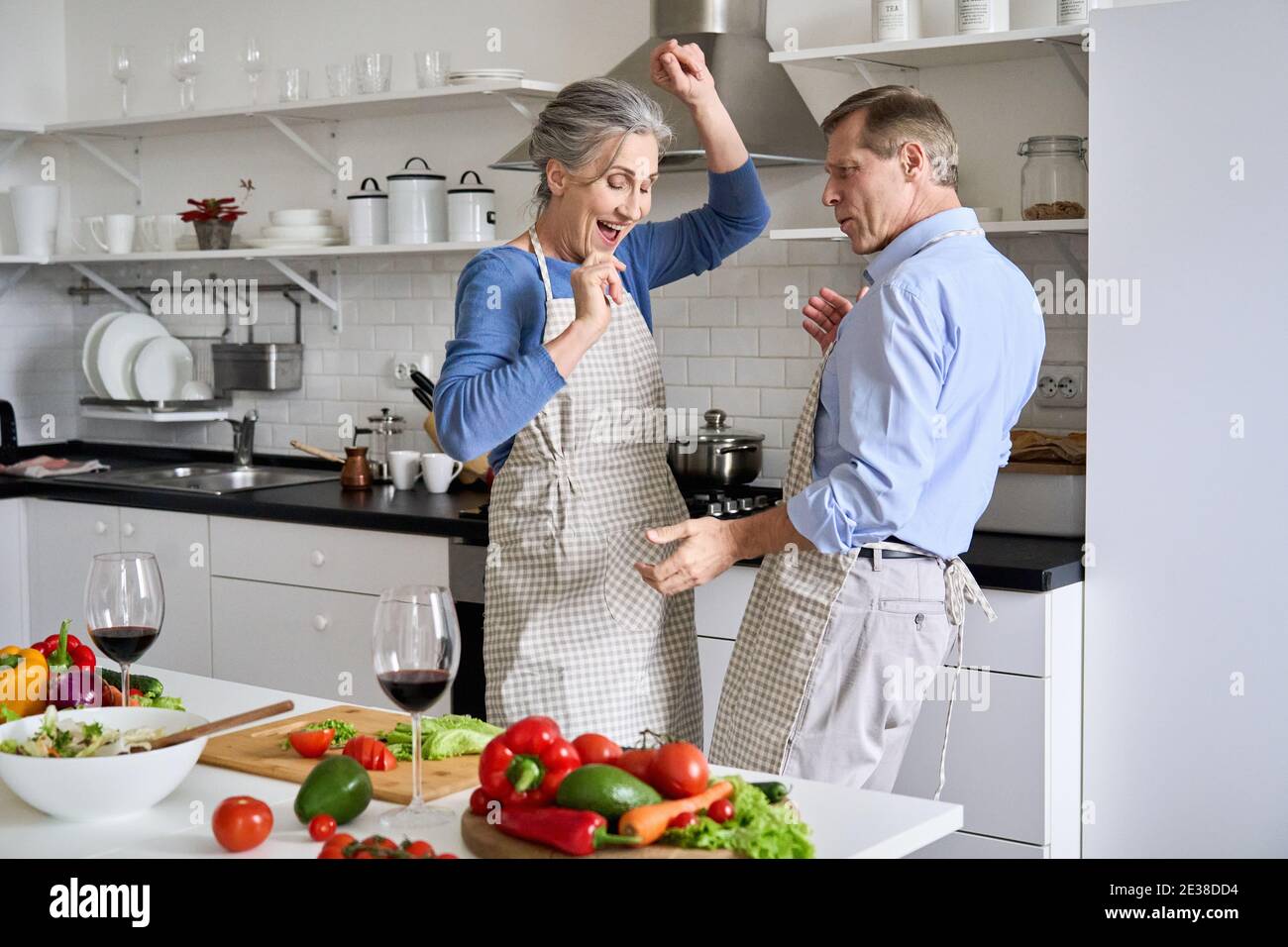 Joyeux vieux couple des années 50 ayant l'amusement dansant la cuisine ensemble dans la cuisine. Banque D'Images