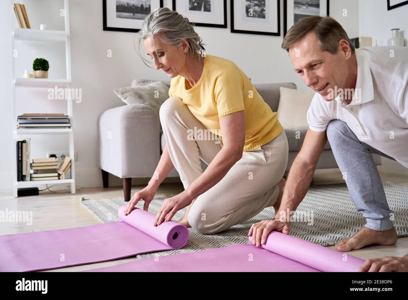 Tenue sportive vieux couple mains roulant ou déroulant Pilates tapis à la maison. Banque D'Images