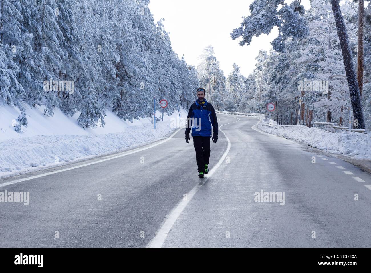 Un homme marche à travers le milieu d'une route sinueuse dans un paysage blanc solitaire enneigé par un froid jour d'hiver.concept de solitude, de liberté et de défi. Banque D'Images