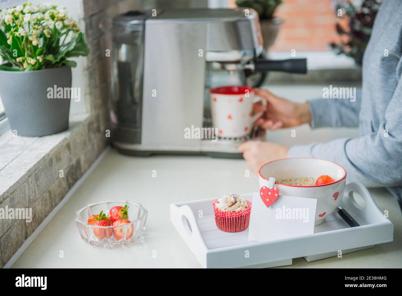 Un plateau avec porridge de flocons d'avoine avec des fraises, un cupcake, et une carte de vœux vierge avec le fond d'une femme faisant du café sur la machine pendant la préparation Banque D'Images