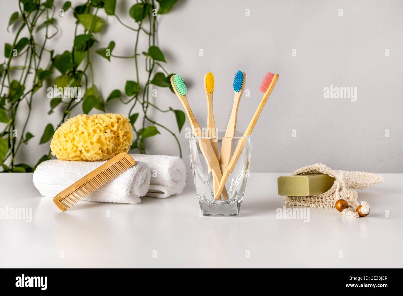 Accessoires de salle de bain écologiques : brosse à dents en bambou, éponge de mer naturelle, savon dans un sac de protection biologique et combiné en bois sur table blanche, plante verte. Zéro Banque D'Images