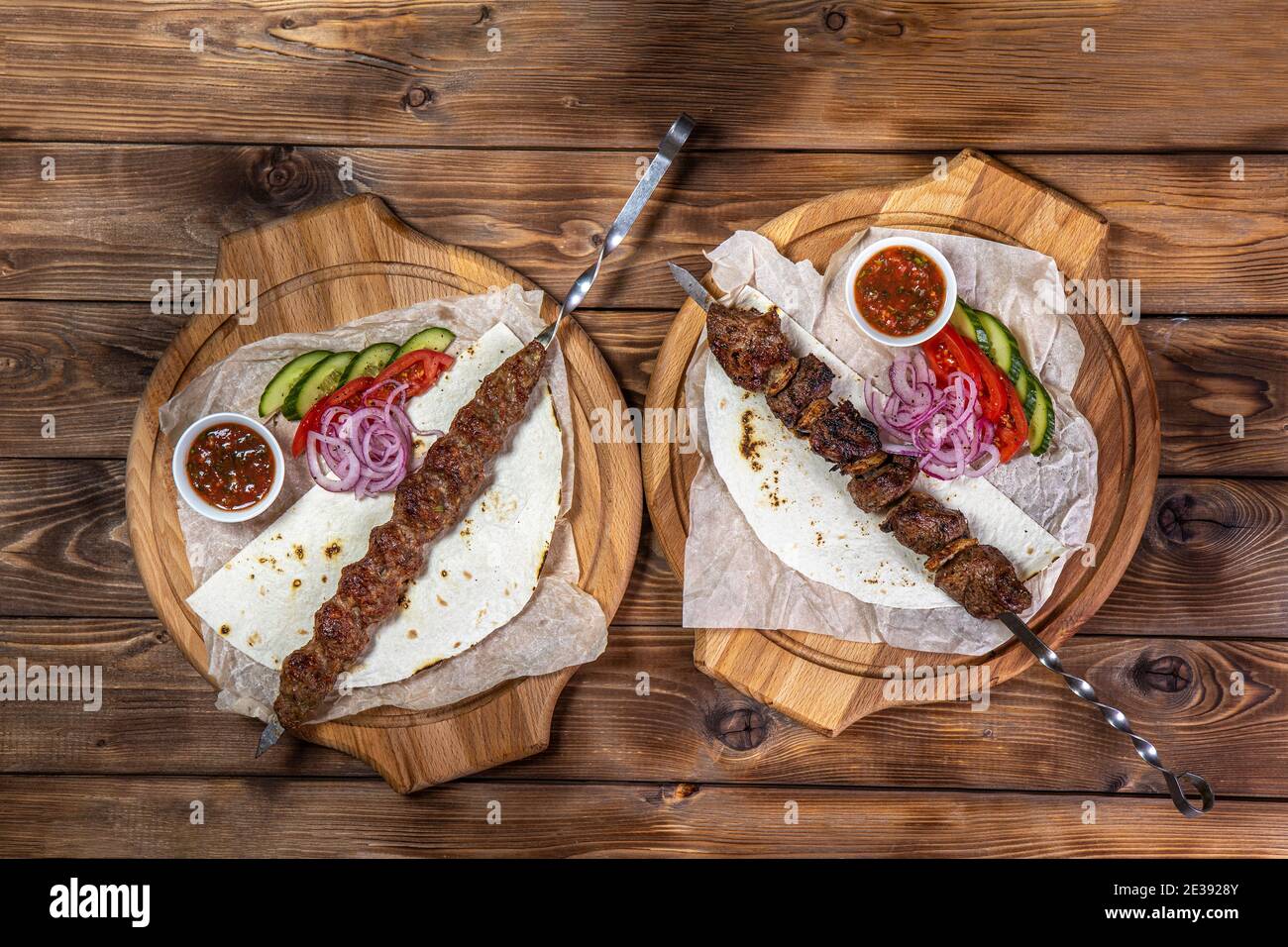 Émincé de kebab sur une brochette de métal avec sauce, tranches de concombres, tomates et oignons sur un plateau en bois Banque D'Images
