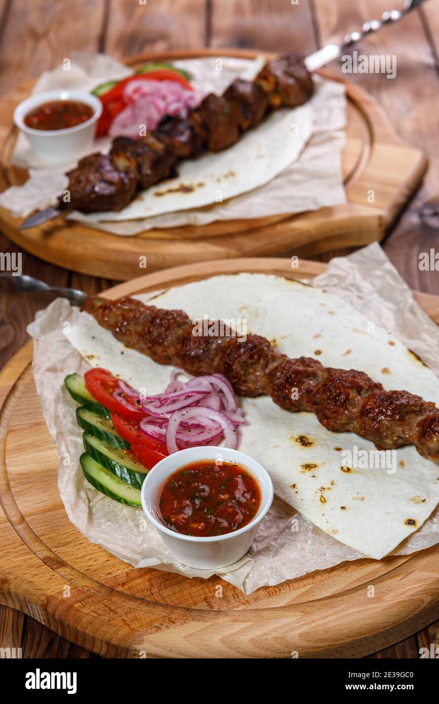 Émincé de kebab sur une brochette de métal avec sauce, tranches de concombres, tomates et oignons sur un plateau en bois Banque D'Images