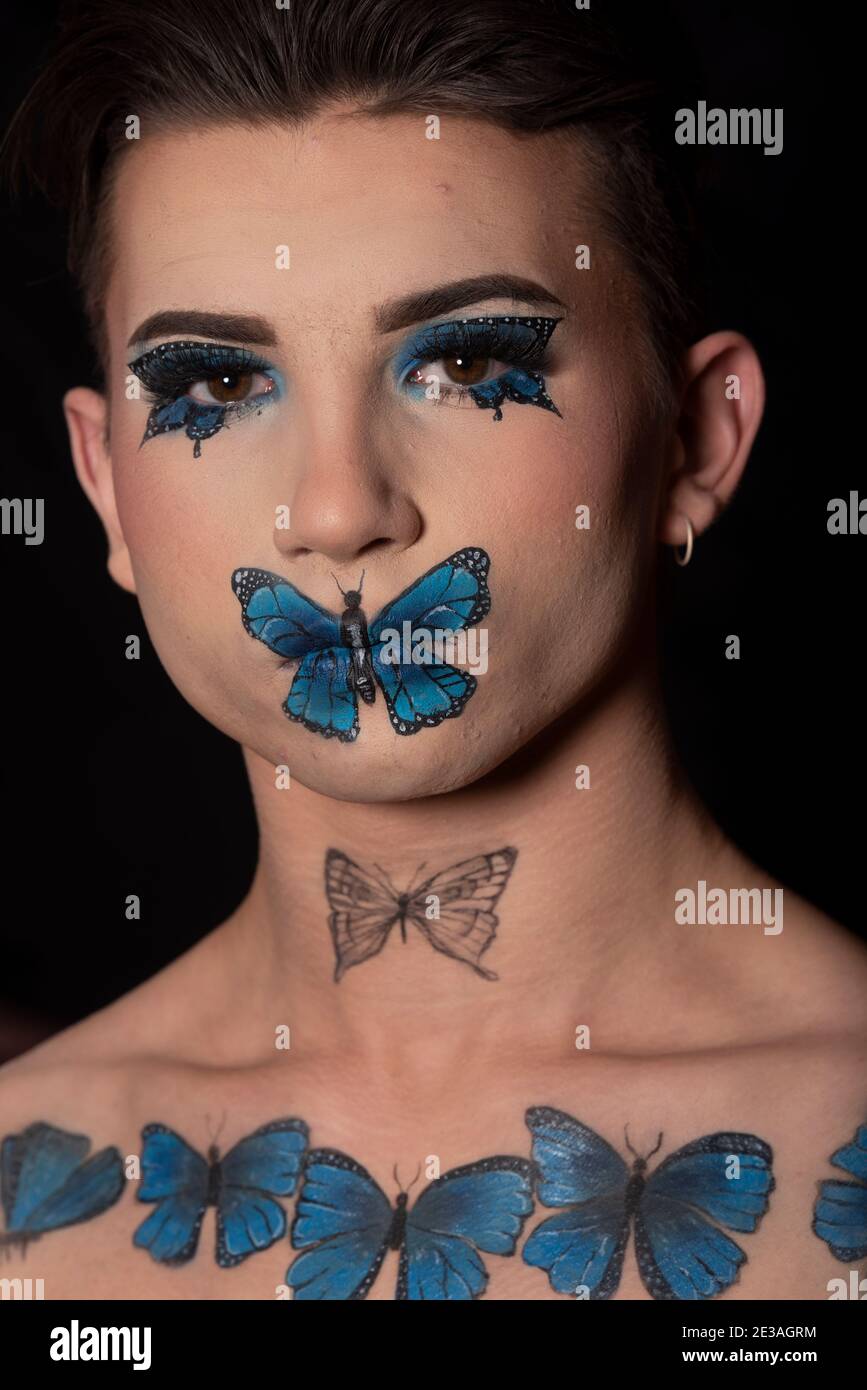 jeune homme modèle avec maquillage artistique de papillons bleus un arrière-plan noir Banque D'Images