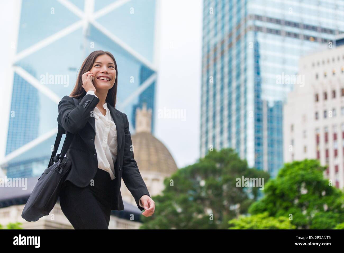 Femme d'affaires asiatique parlant sur un téléphone mobile marchant dans la ville de Hong Kong rue à bureau, gratte-ciel fond urbain. Jeune femme sur smartphone Banque D'Images