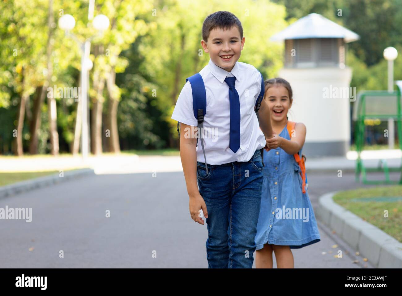 Joyeux écoliers fille et garçon dans une chemise blanche avec sacs à dos le matin par beau temps en été Banque D'Images