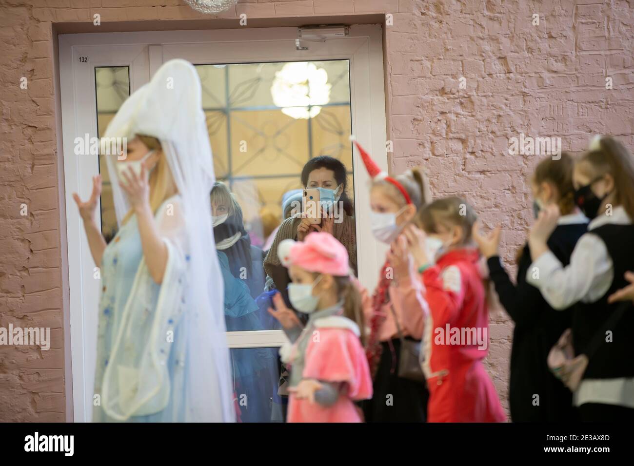 24 décembre 2020. Biélorussie, la ville de Gomil. Vacances de Noël dans la ville. Les parents dans des masques médicaux regardent par une porte en verre une fête d'enfants d Banque D'Images