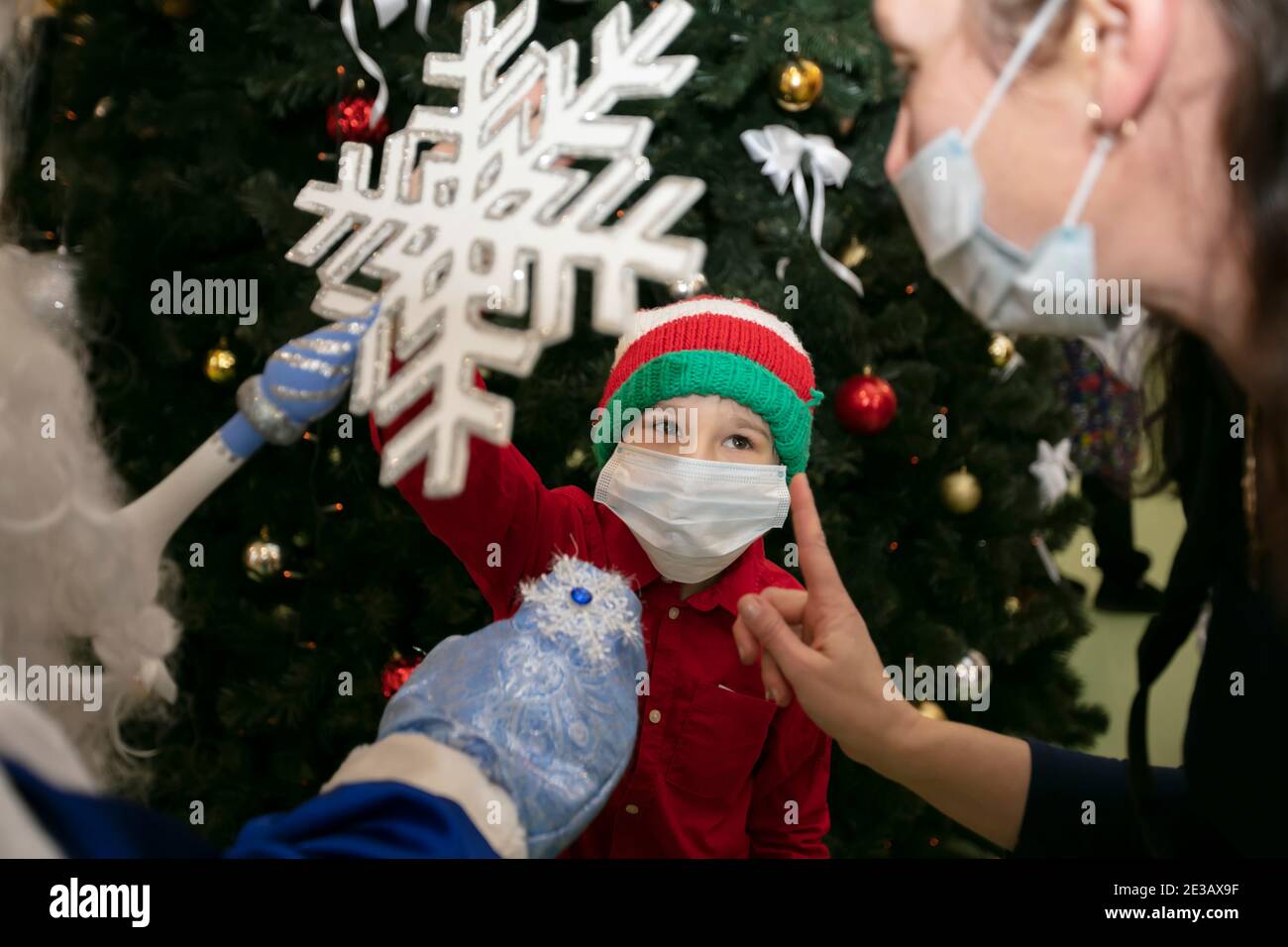 Un enfant dans un masque médical et un chapeau du nouvel an tient un flocon de neige du Père Noël dans sa main pendant la pandémie du coronavirus. Le garçon fait un souhait à Sant Banque D'Images