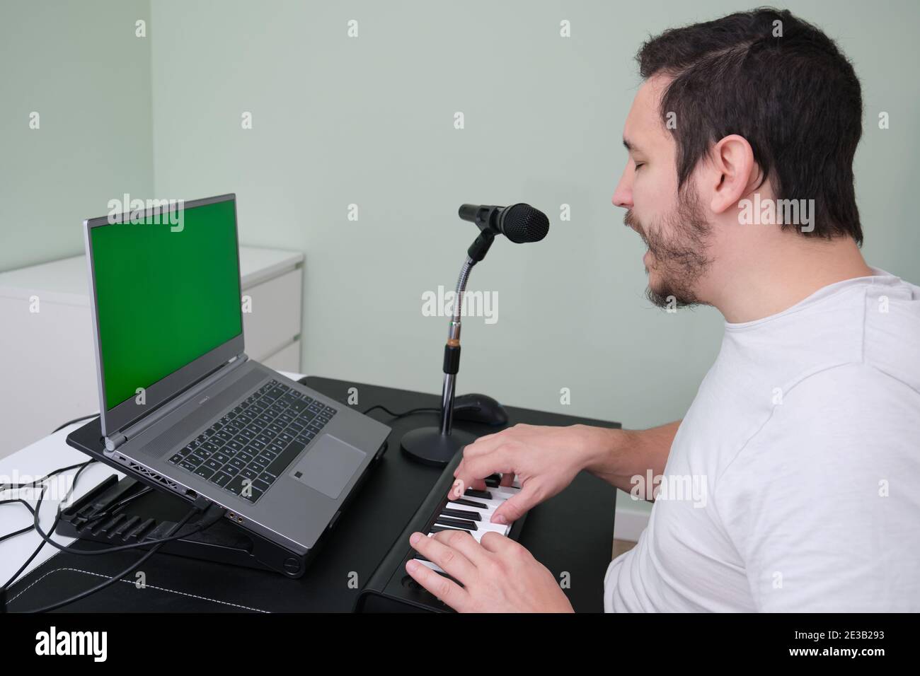 Un homme blogueur, youtuber, influenceur enregistrant une vidéo jouant le piano électronique et chantant à la maison. Musicien, chanteur, pianiste. Écran vert o Banque D'Images