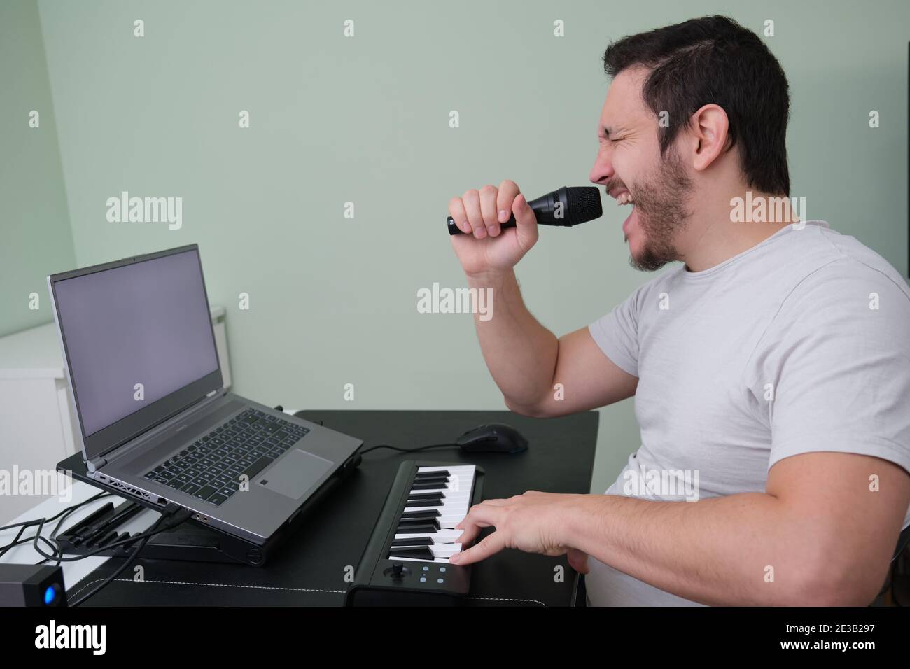 Un homme blogueur, youtuber, influenceur enregistrant une vidéo jouant le piano électronique et chantant à la maison. Musicien, chanteur, pianiste. Écran blanc o Banque D'Images